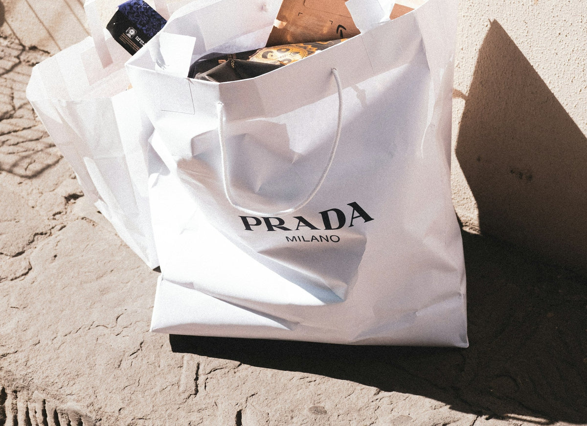 Full Prada shopping bag sitting on the floor against a sunlit wall
